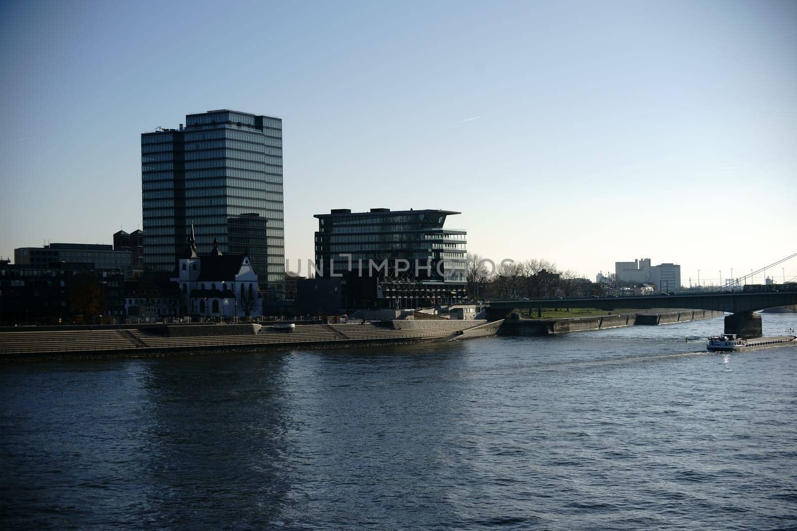 The Lanxess skyscraper at the Severins Bridge in Cologne with a passing cargo ship.