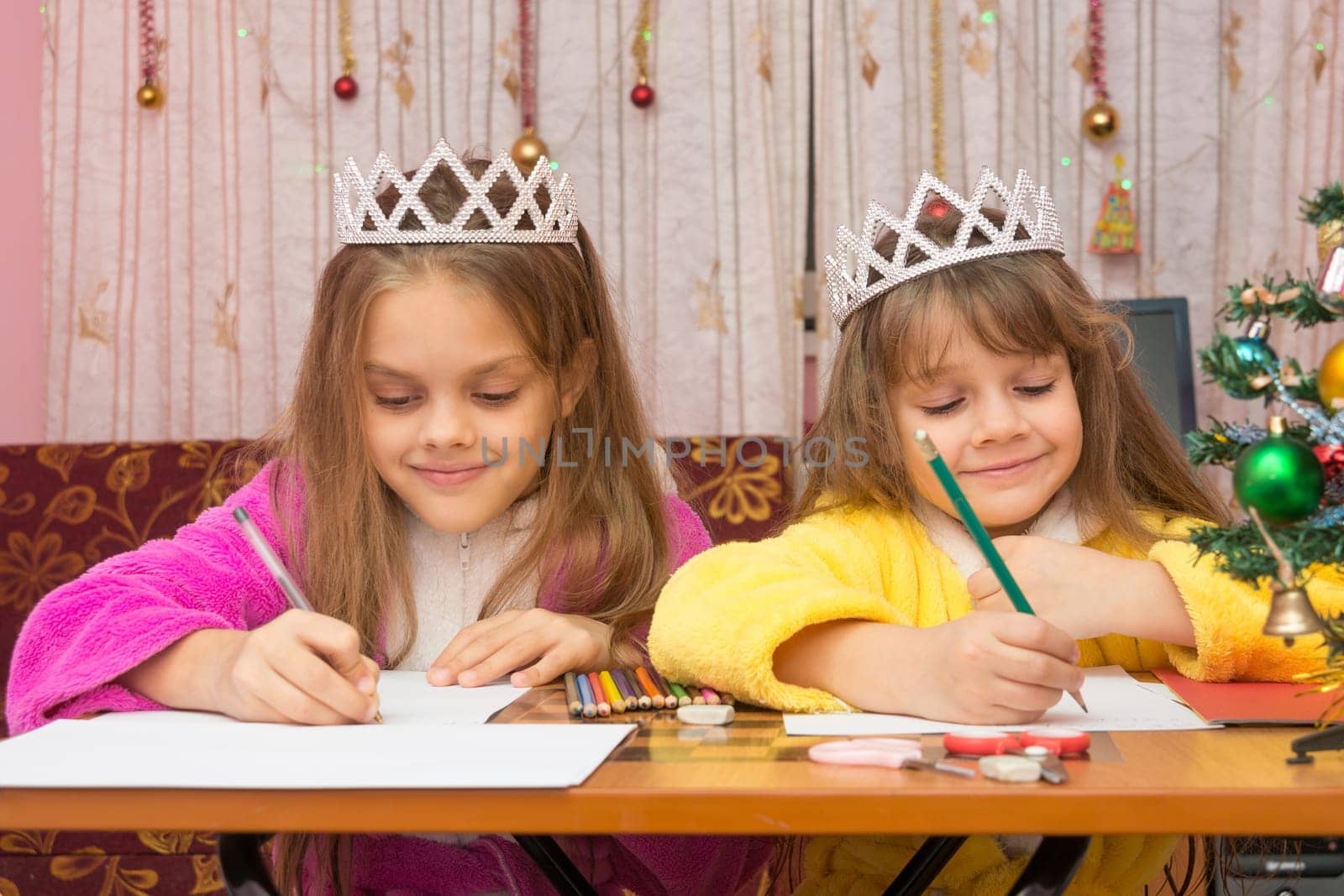Two girls happily writing a letter to Santa Claus sitting at a desk in the home environment