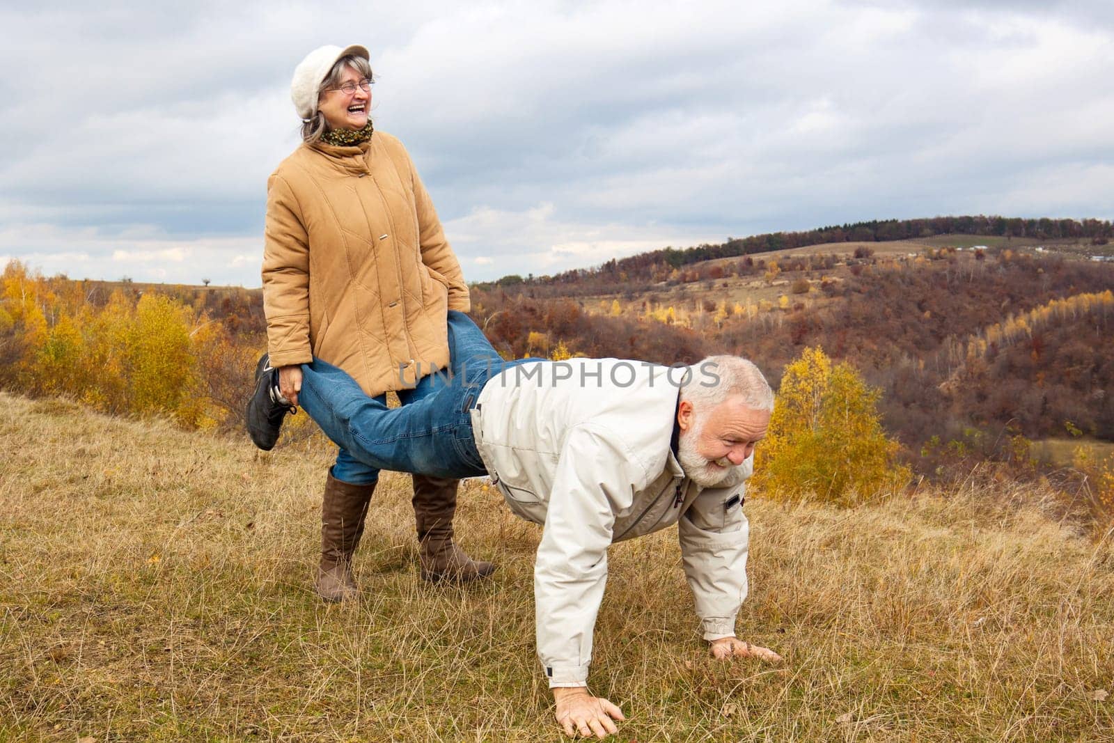Elderly couple having fun and playing the wheelbarrow in nature.  "Woman carried his husband until old age."""