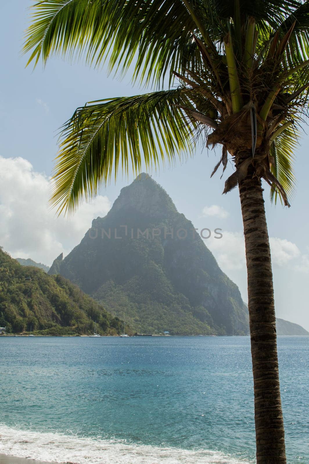 Beach view across the bay at Soufriere to the sea and Piton mountain. Framed with a palm tree