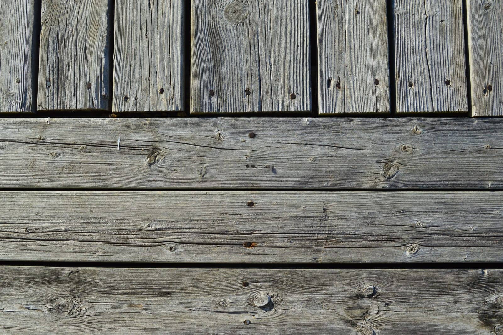 Silvery weather worn wooded planks on an old dock run both horizonally and vertically as a background with character