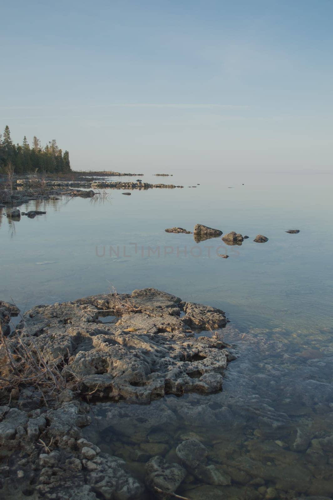 Dead calm afternoon image of clear lake huron water and limestone rocks along shoreline.