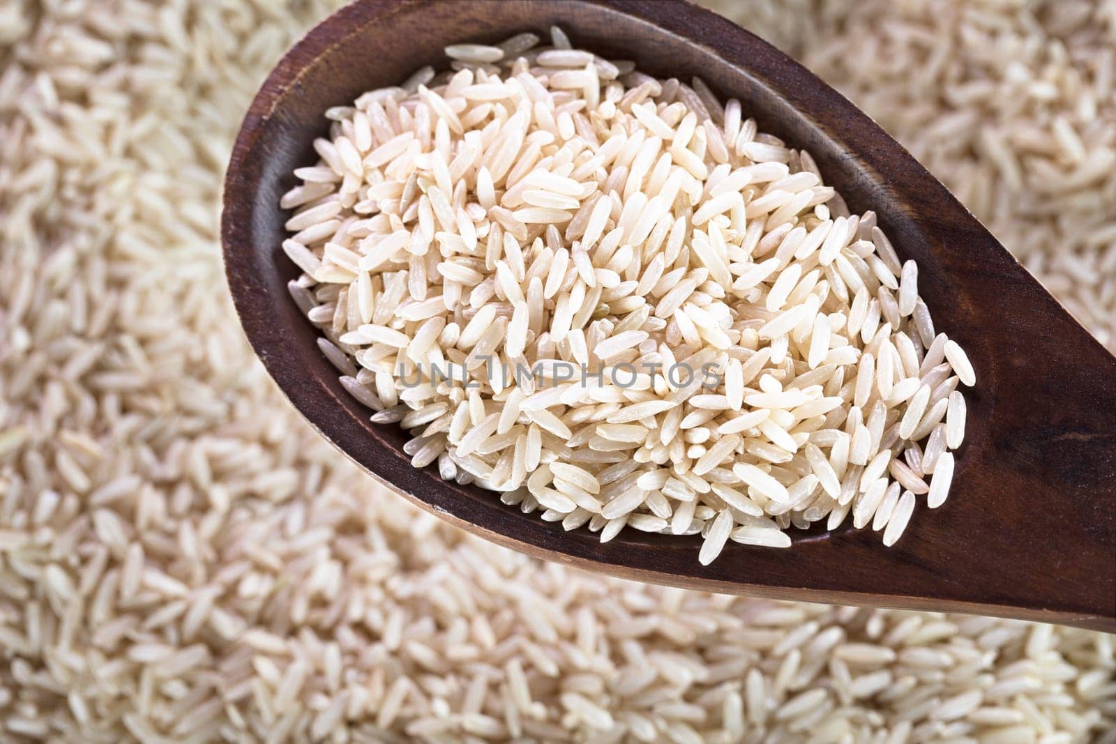 Wooden spoon full of brown rice.