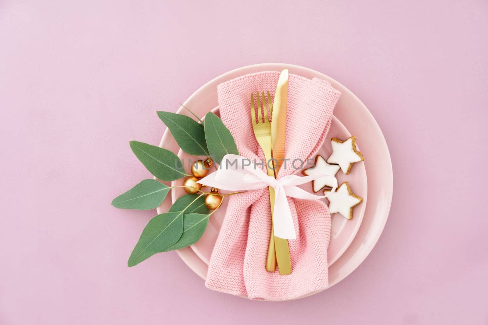 Christmas place setting in pink with golden silverware, eucalyptus and cinnamon stars