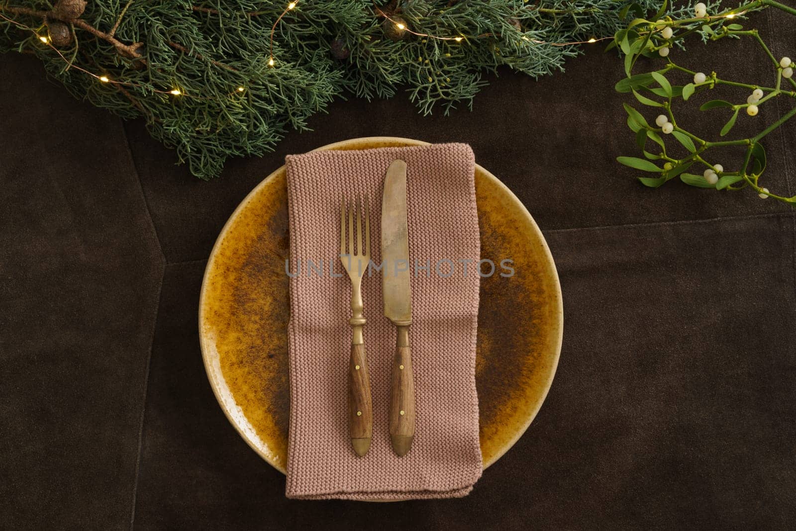 Christmas place setting with brown plate, mistletoe, fir green and fairy lights