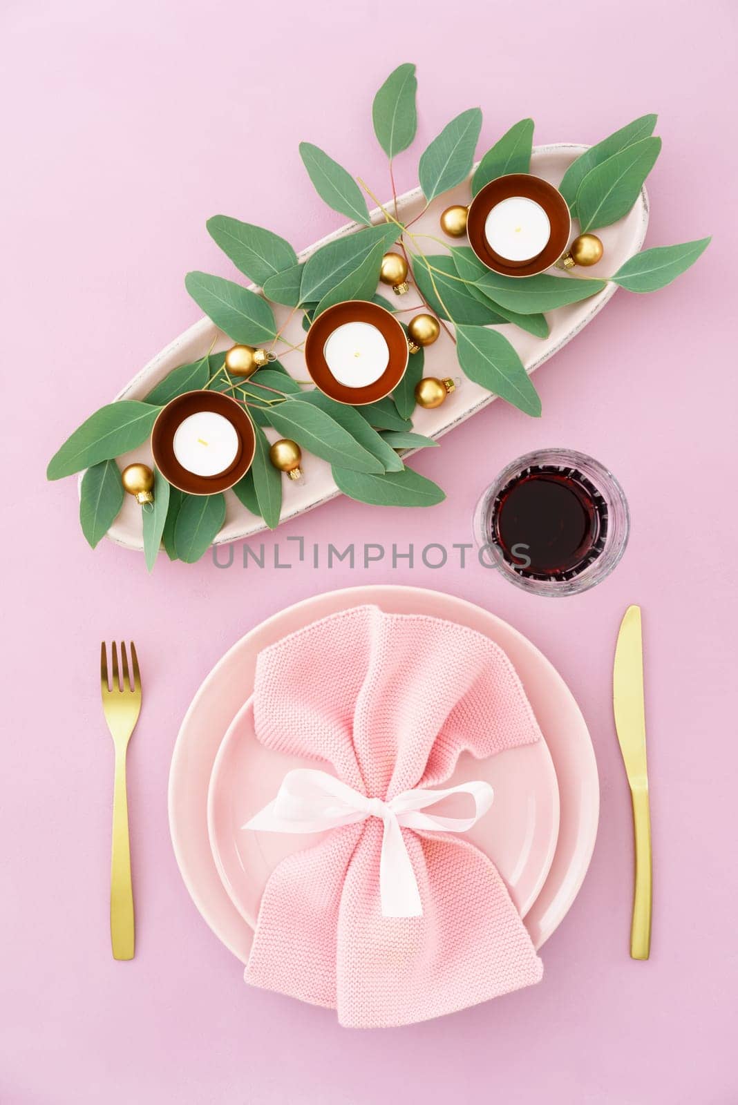 Christmas place setting in pink with golden silverware, eucalyptus and candles
