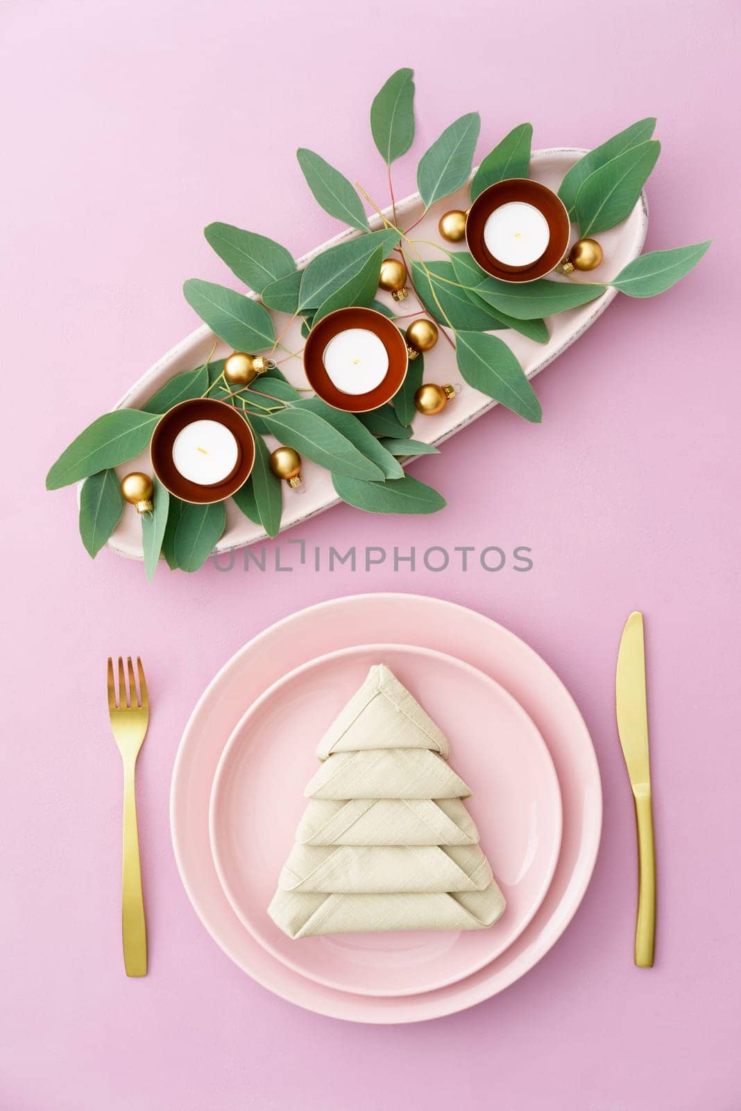 Christmas place setting in pink with golden silverware, eucalyptus and candles