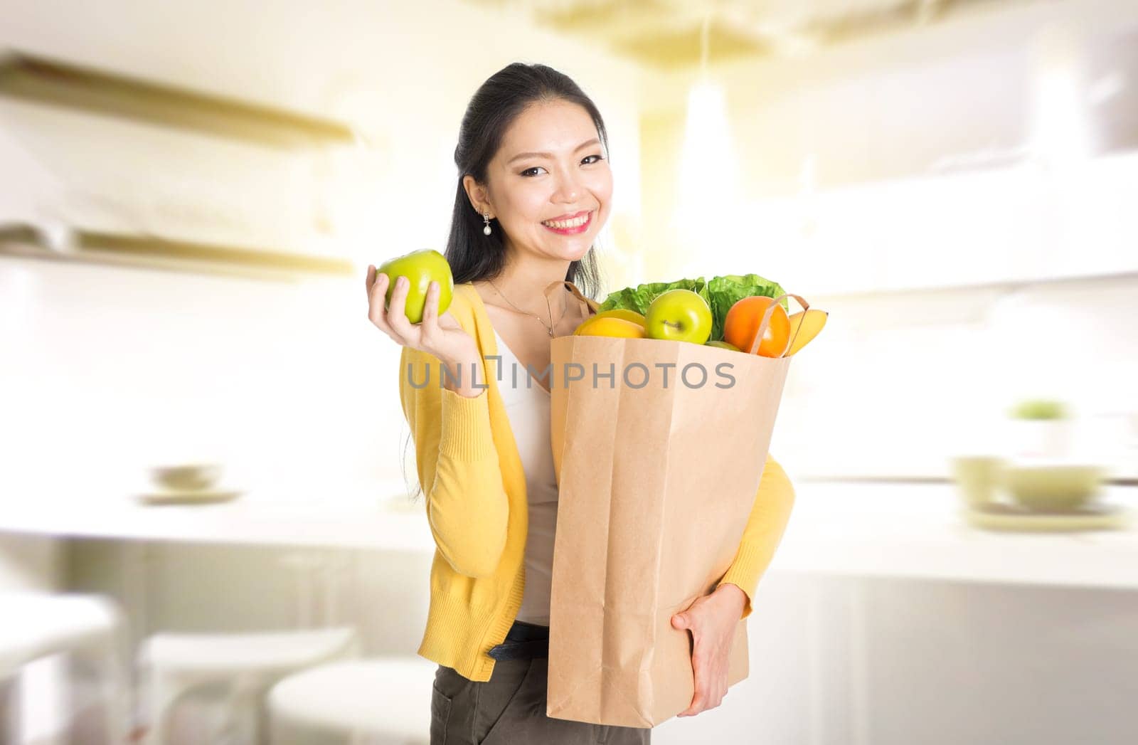 Young Asian female hand holding shopping paper bag filled with fruits and vegetables in kitchen.