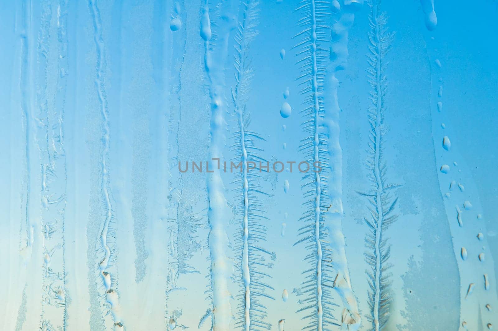 Melted and frosted ice pattern on frosty window glass in winter