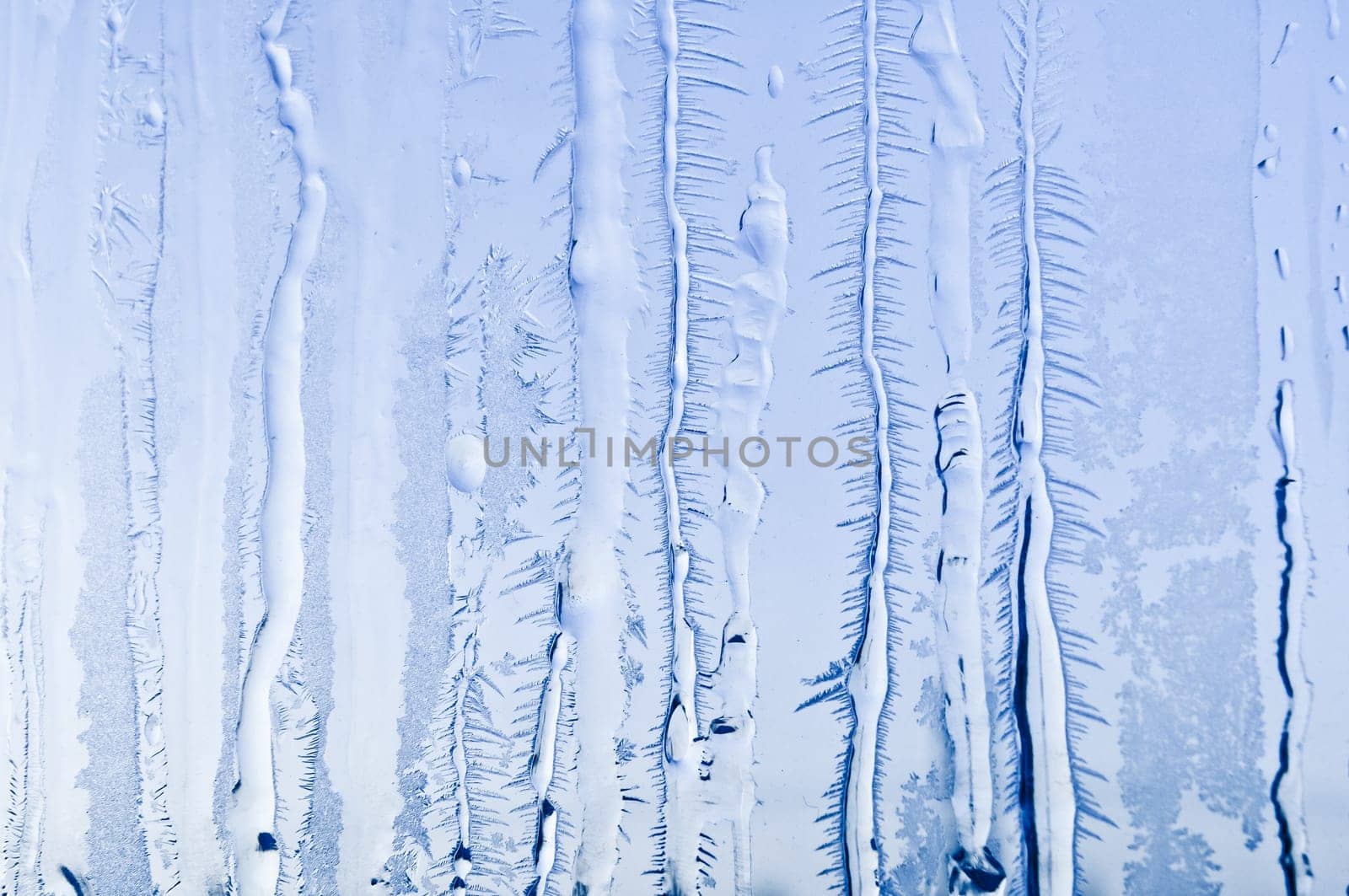 Melted and frosted ice pattern on frosty window glass in winter