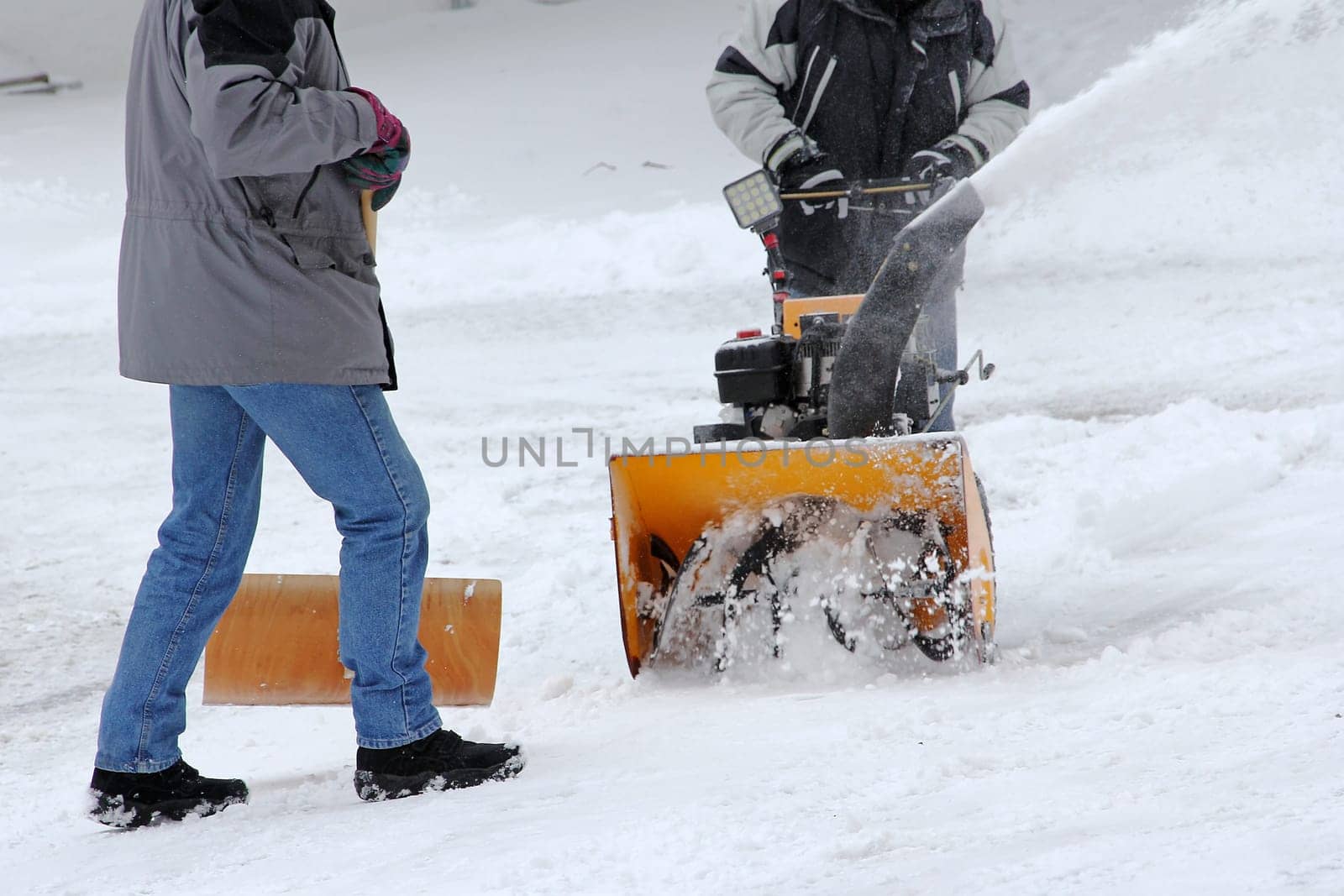 Snow clearing in winter. Two men clear snow from the road. Snow clearing with snow blower and snow shovel