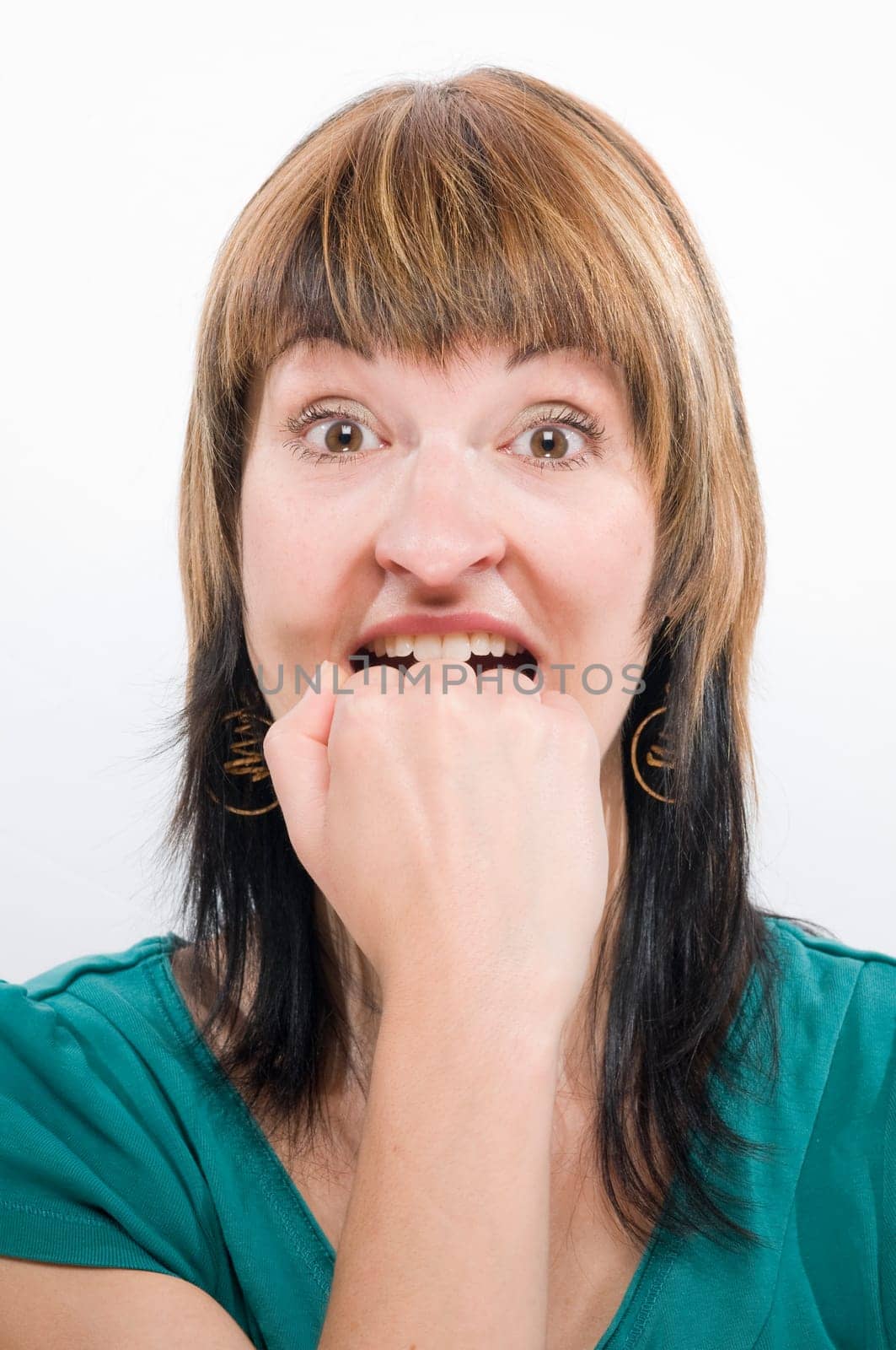 Head portrait of a young brunette woman against a white background,desperately biting her fist.