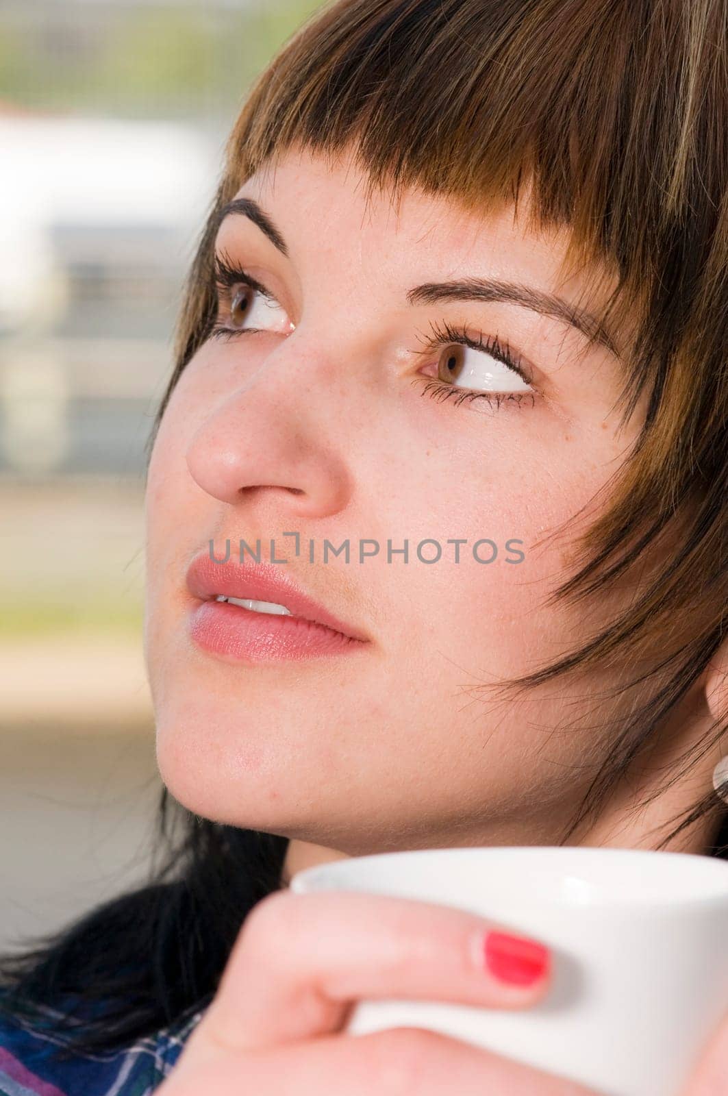 Close up a young woman with a white cup held in front of her mouth looking to the side.