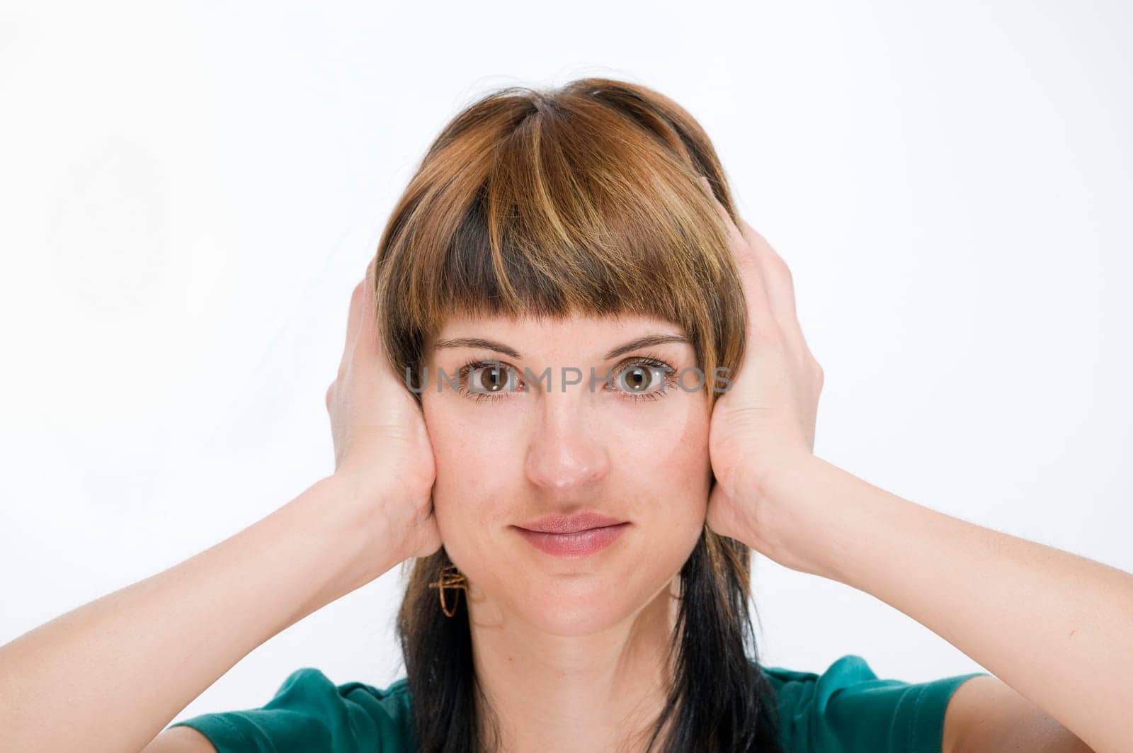 Head portrait of a young brunette woman against a white background holding her ears.