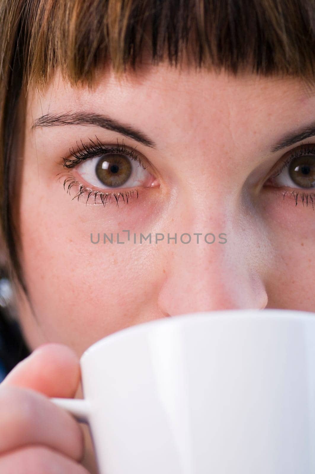 Close up of a young woman with a white cup held in front of her mouth.