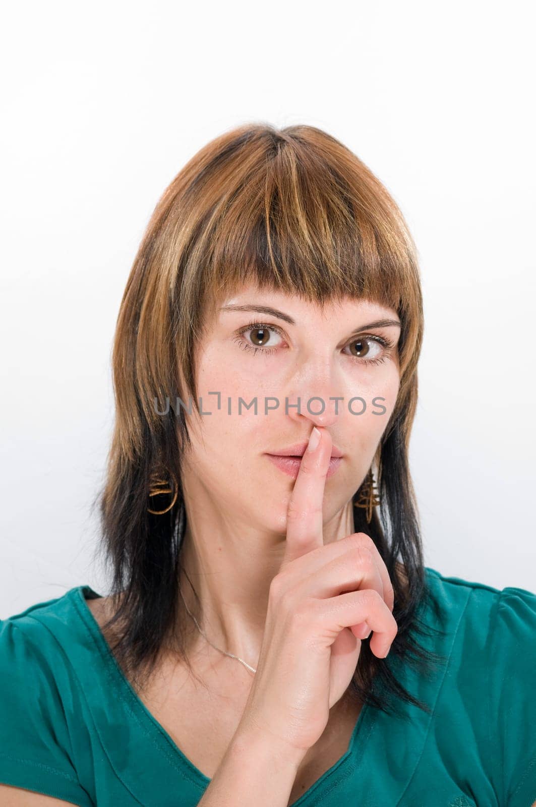 Head portrait of a young brunette woman against a white background laying her finger on her mouth.
