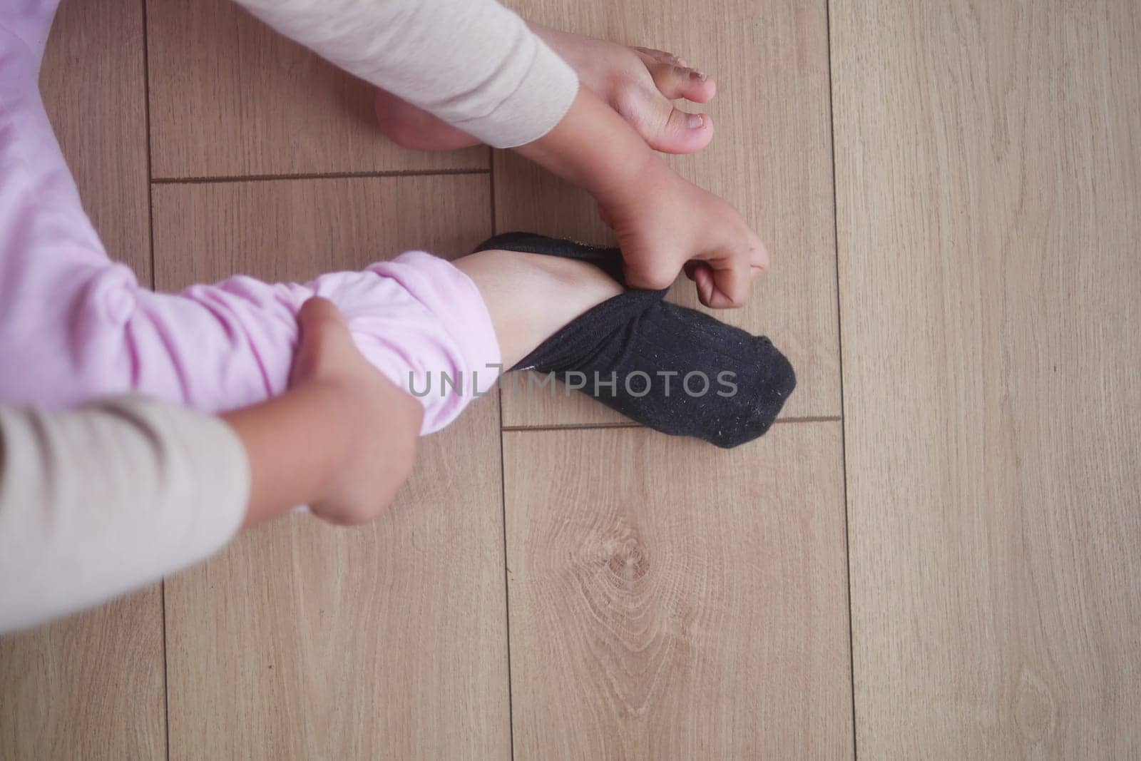 A child is pulling on a black sock while seated on a wooden floor.