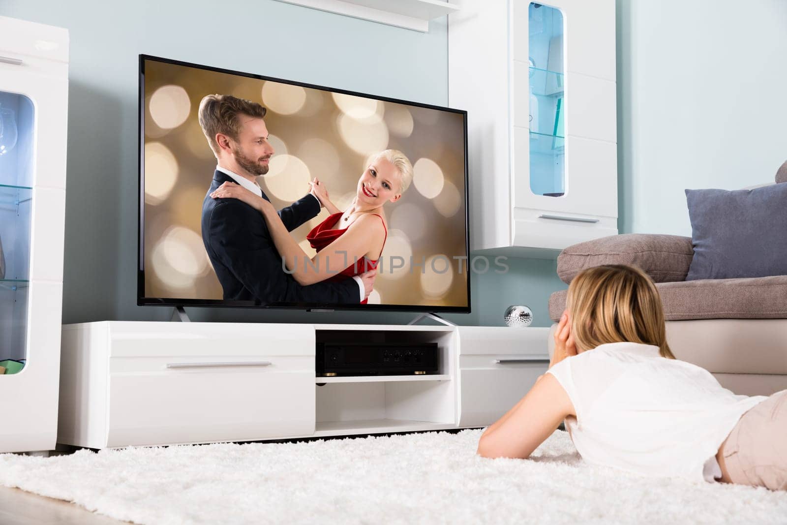 Young Woman Lying On Carpet Watching Romantic Movie On Television At Home