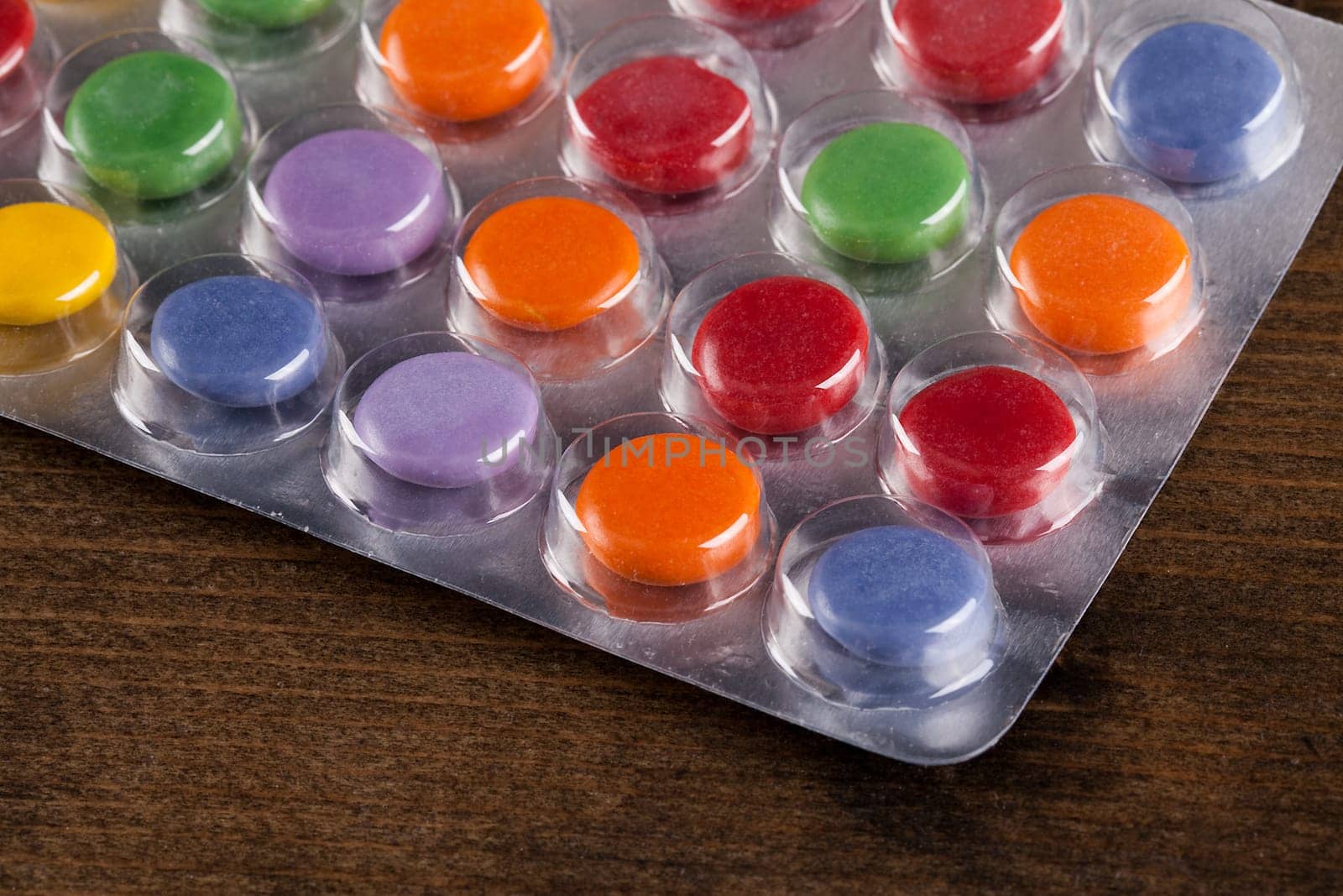 Pills in a bubble pack viewed at an angle. Bright colours and round tablets sealed under plastic, on a wooden table