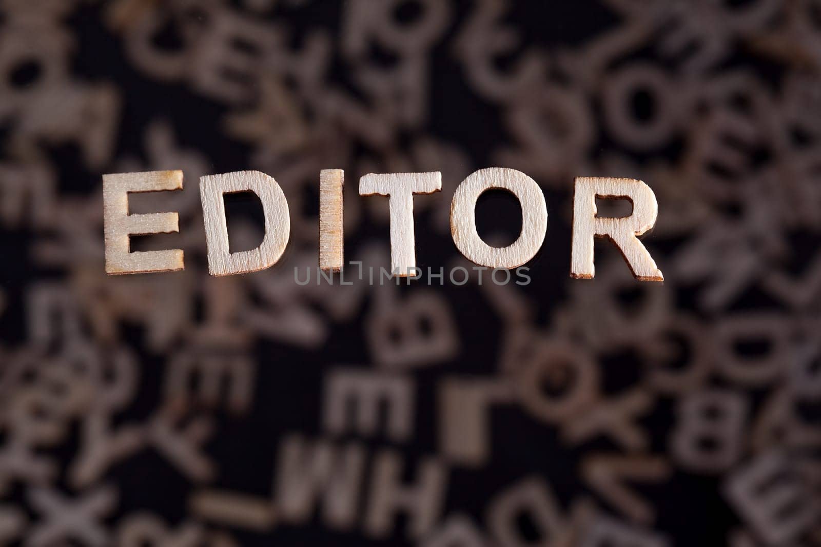 Editor wooden letters created in wood floating above random letters below out of focus on a black background