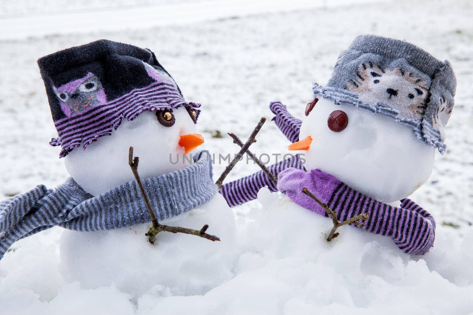 Two cute snowmen dressed for winter in scarfs and hats embracing each other as long lost friends. Winter scene with snow.