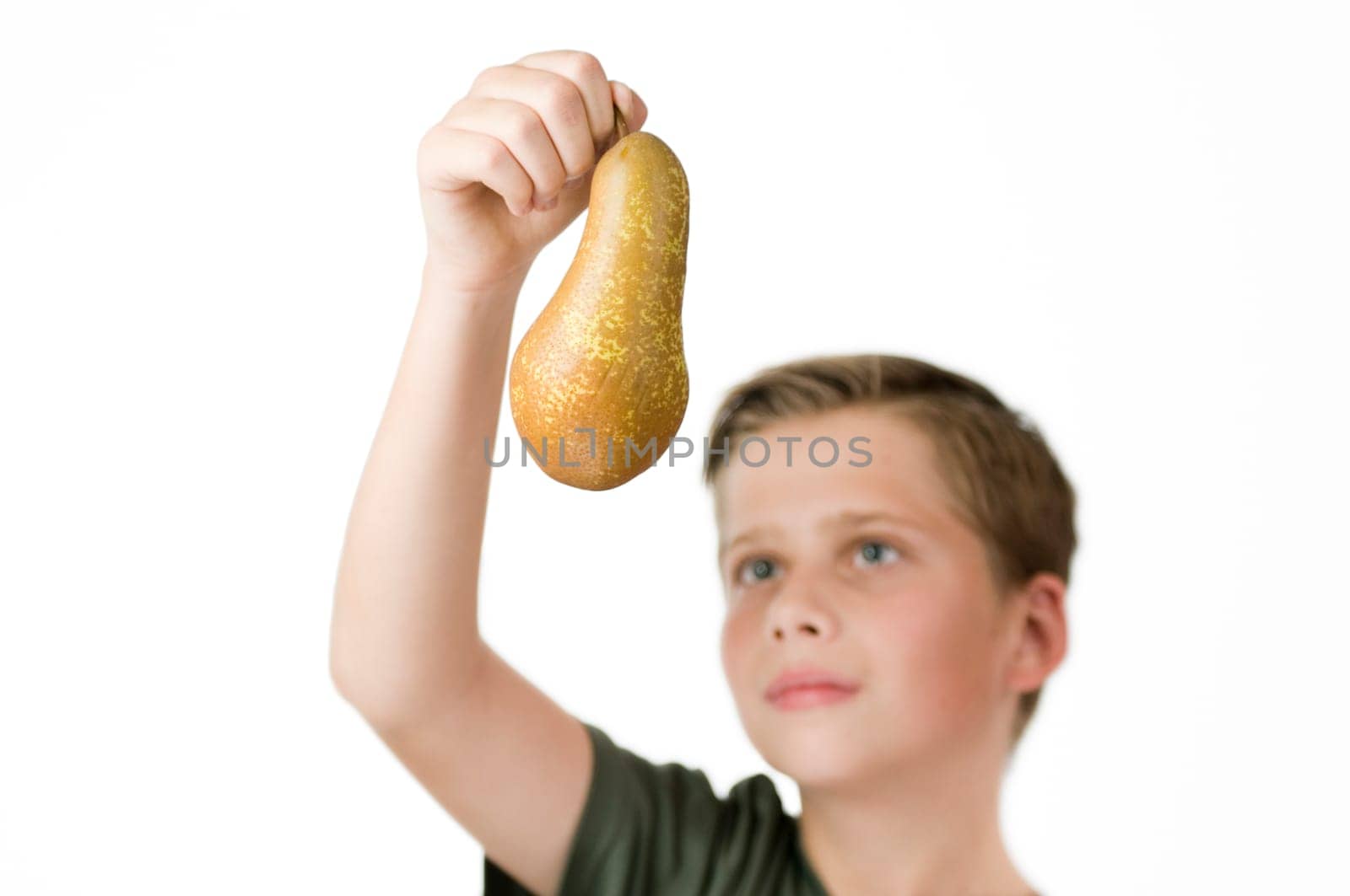 Frontal head and shoulder view of a young male teenager against a white background with his right hand holding up a pear in front of him