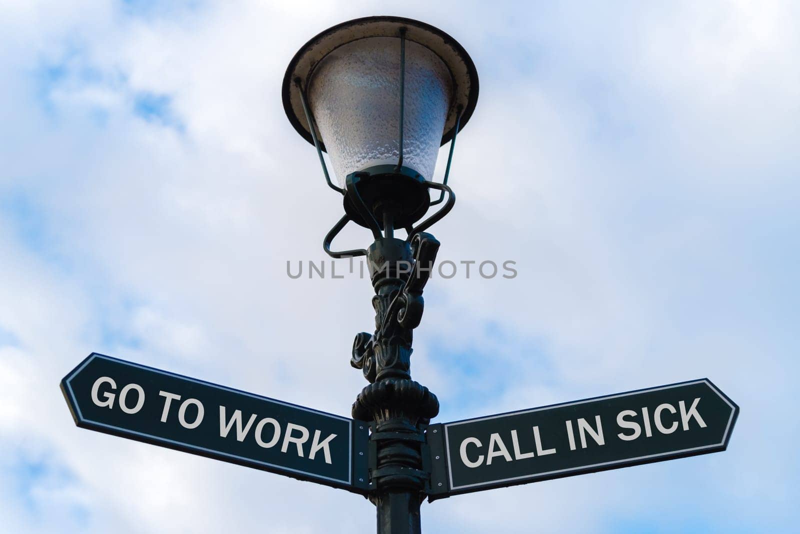 Street lighting pole with two opposite directional arrows over blue cloudy background. Go To Work versus Call In Sick concept.