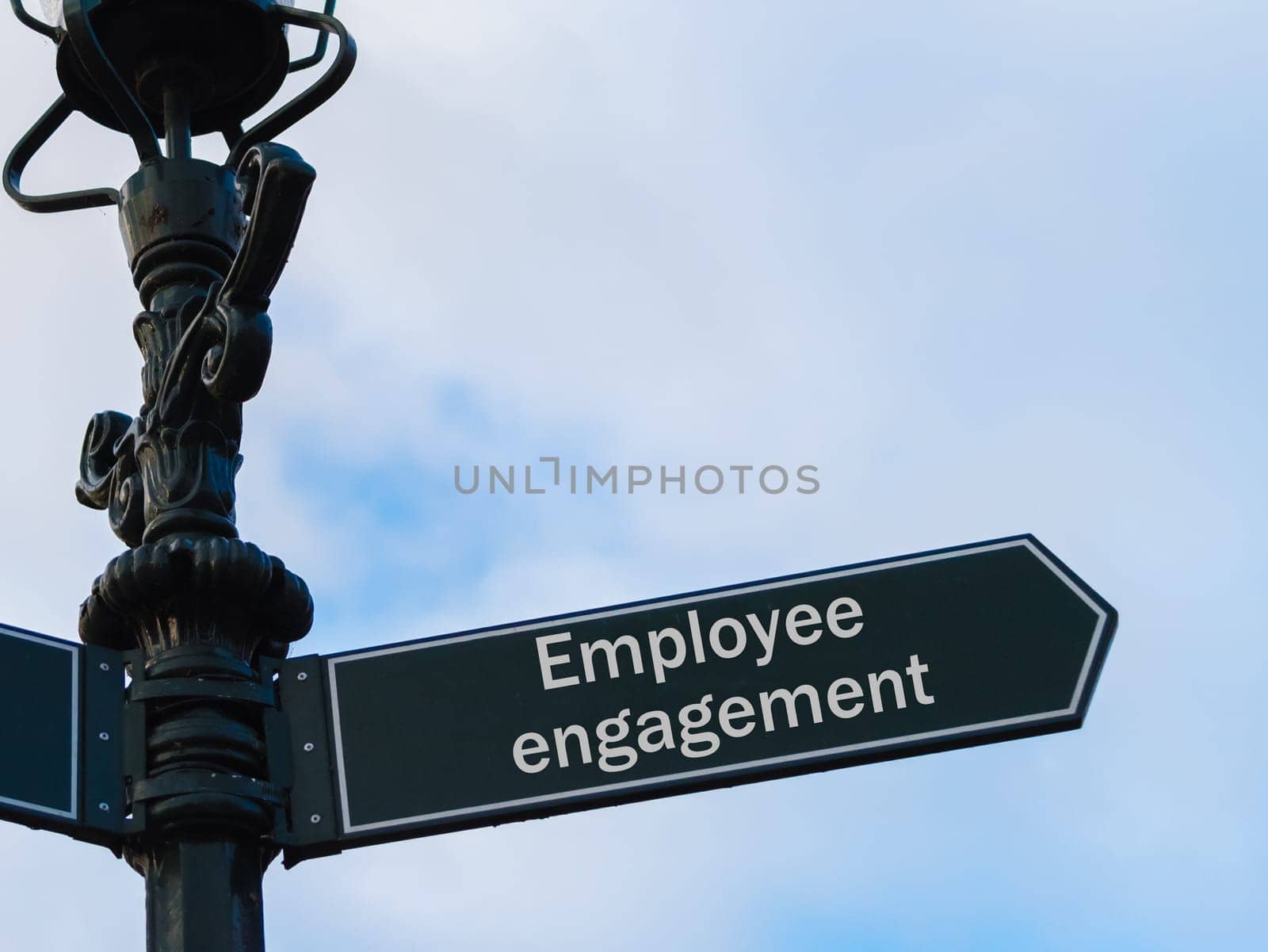 Street lighting pole with conceptual message Employee Engagement on directional arrow over blue cloudy background.