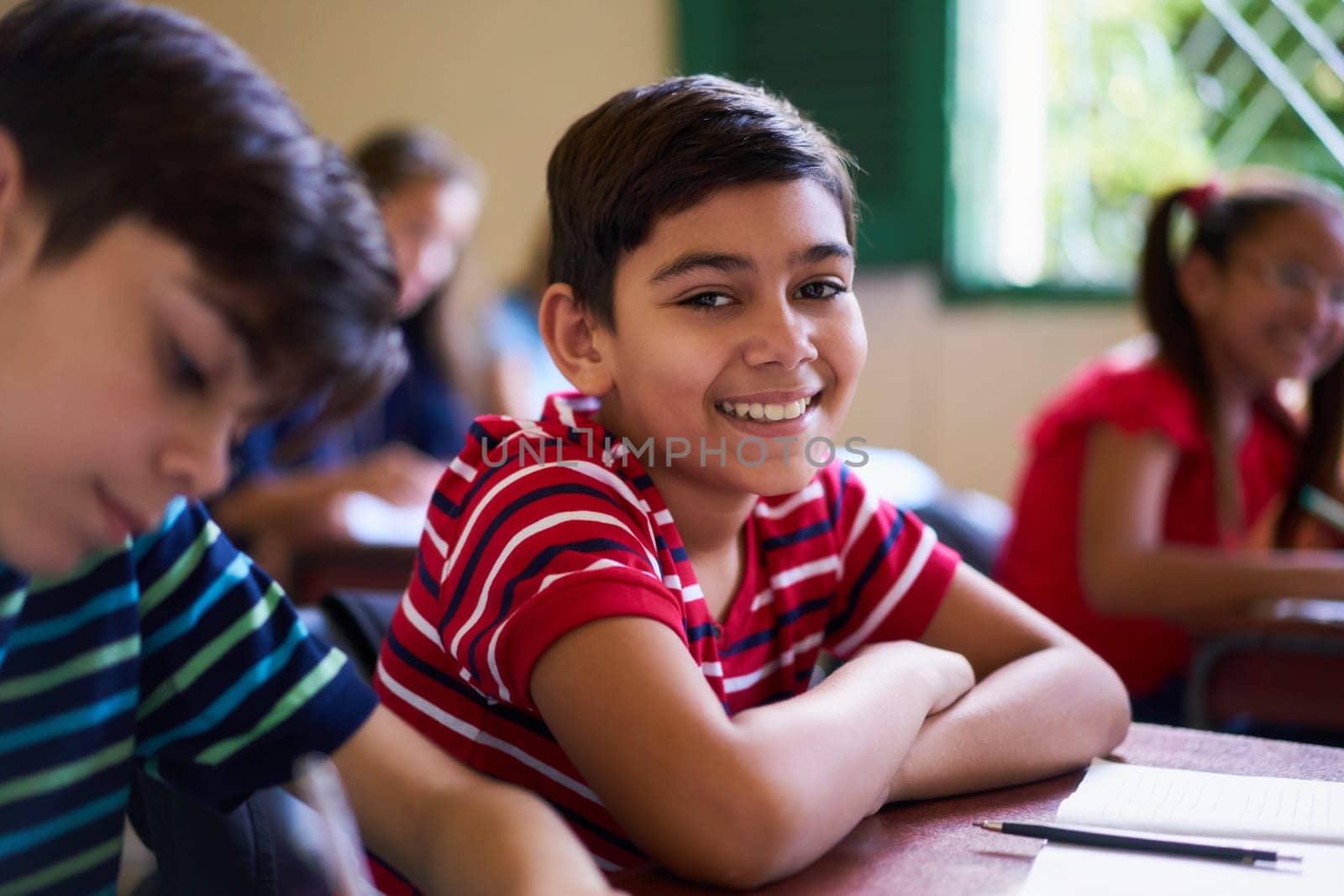 Young people and education. Group of hispanic students in class at school during lesson. Happy boy smiling and sitting at desk