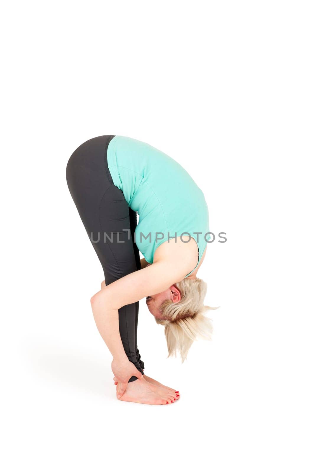 Full-body view of a young blonde woman during yoga exercise "Standing Prevention"" Step 3 against a white background with a slight shadow"