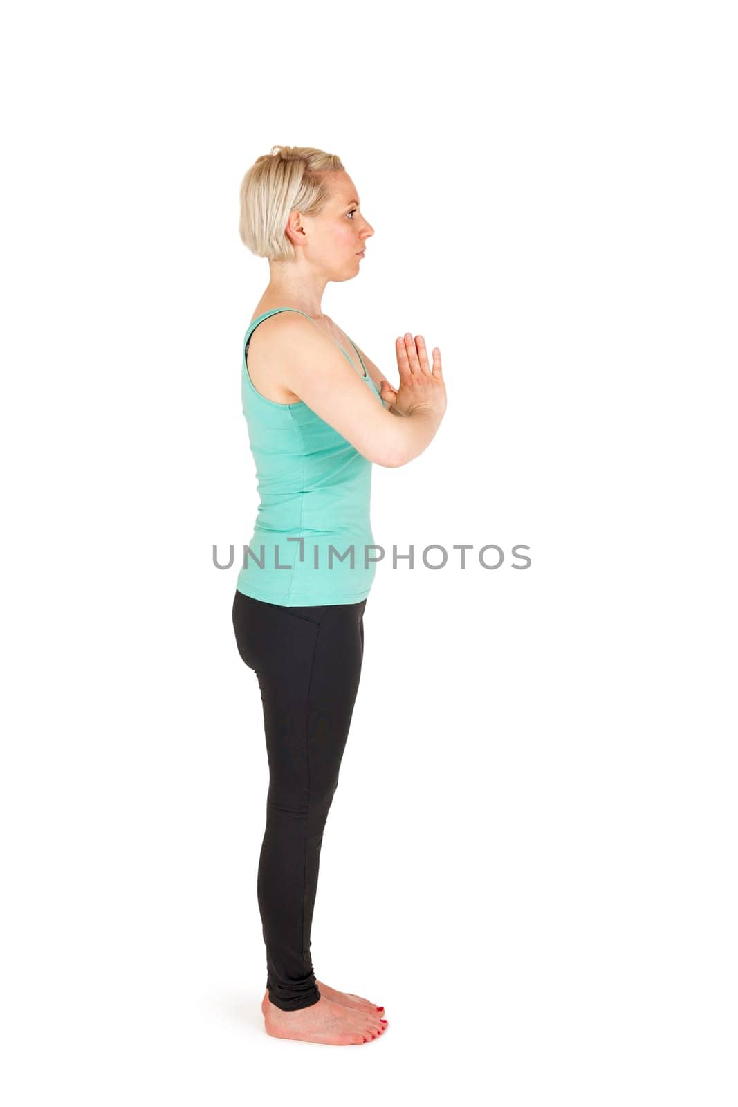 Full-body view of a young blonde woman during yoga exercise "Standing Prevention"" Step 1 against a white background with a slight shadow"