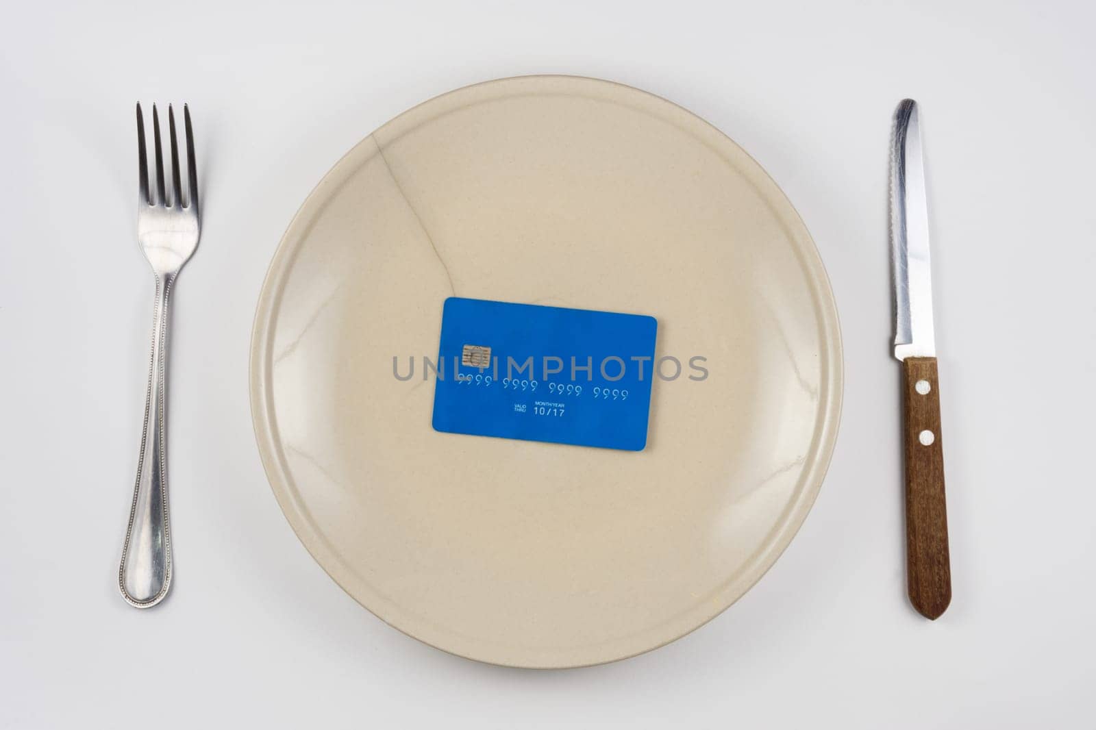 On the cracked plate is a plastic credit card, next lie fork and knife, white background, top view