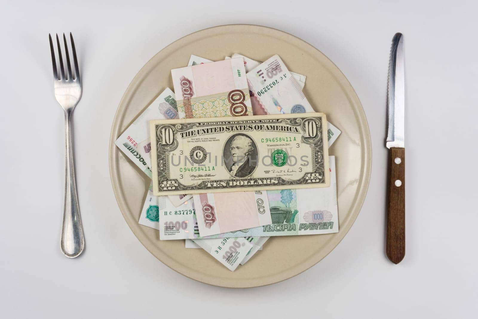 On the plate is a lot of money Russian rubles, they have a ten dollars banknote, lie next to utensils top view