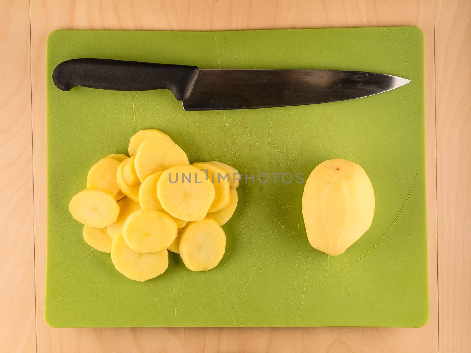 Pattern of sliced peeled potatoes on green used plastic board, simple food preparation illustration, vegetarian dieting, still life with center composition, close up