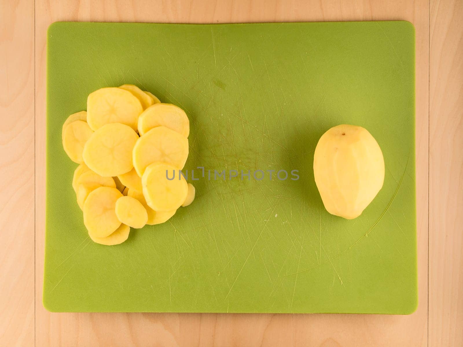 Pattern of sliced peeled potatoes on green used plastic board, simple food preparation illustration, vegetarian dieting, still life with center composition, close up