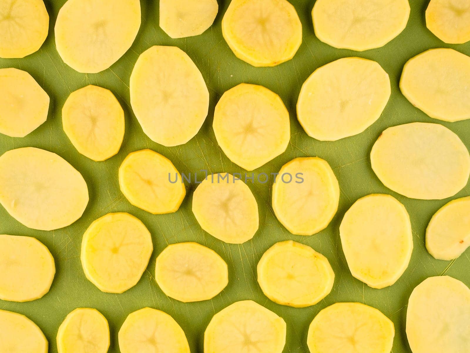 Pattern of sliced peeled potatoes on green used plastic board, simple food preparation illustration, vegetarian dieting, still life with center composition, close up