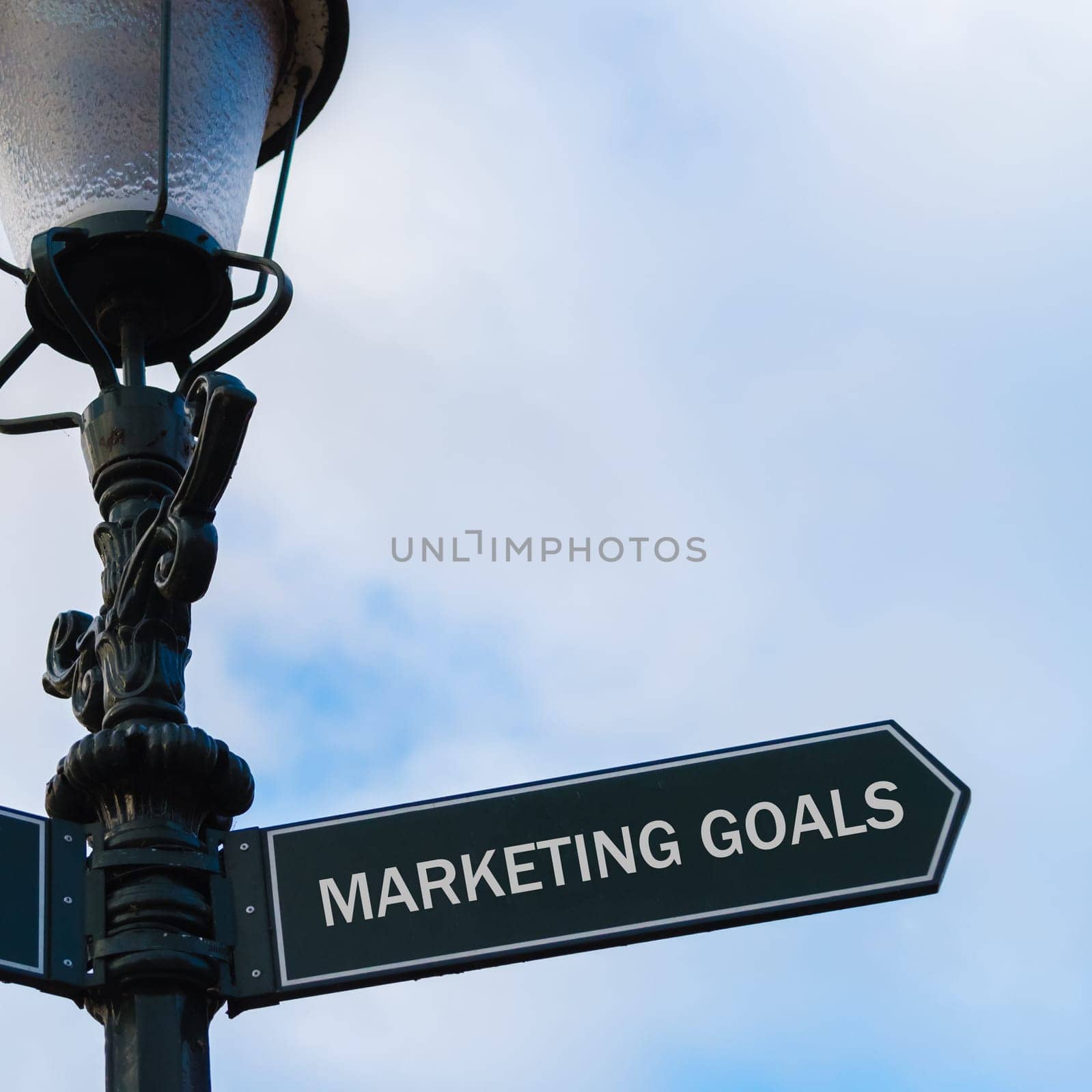 Street lighting pole with conceptual message MARKETING GOALS on directional arrow over blue cloudy background.