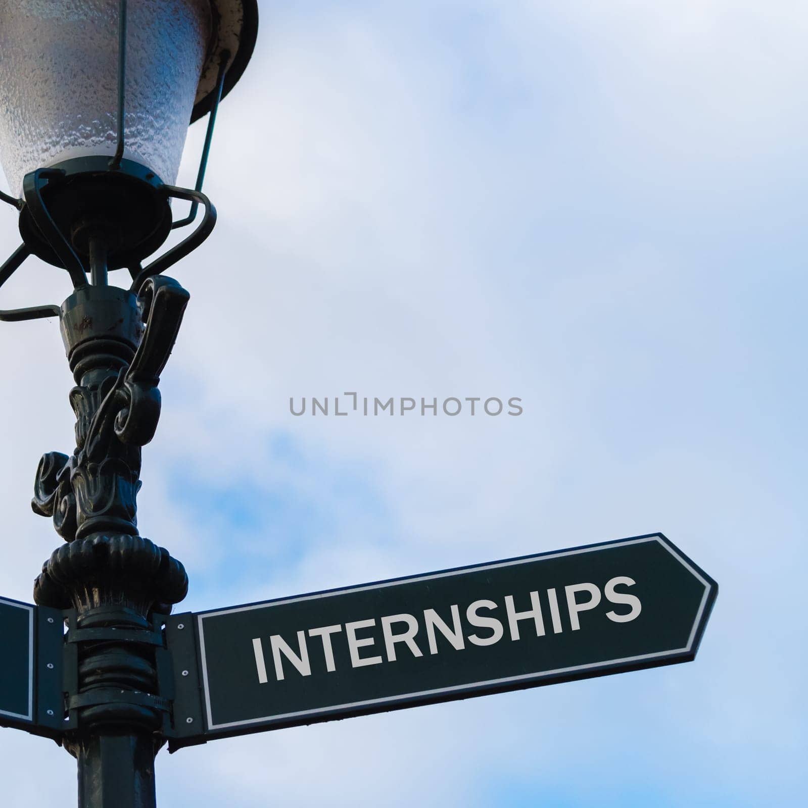 Street lighting pole with conceptual message INTERNSHIPS on directional arrow over blue cloudy background.