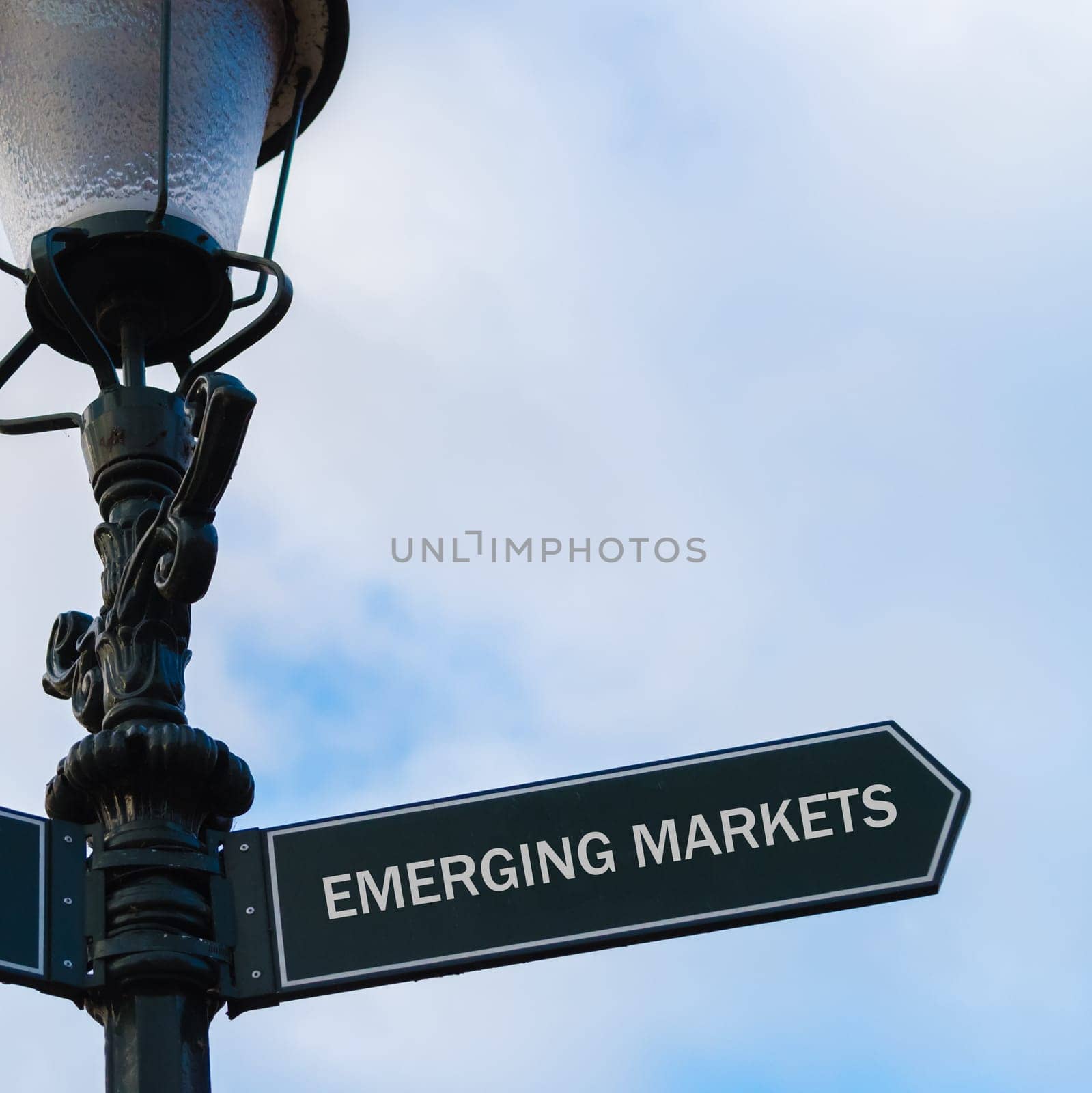 Street lighting pole with conceptual message EMERGING MARKETS on directional arrow over blue cloudy background.