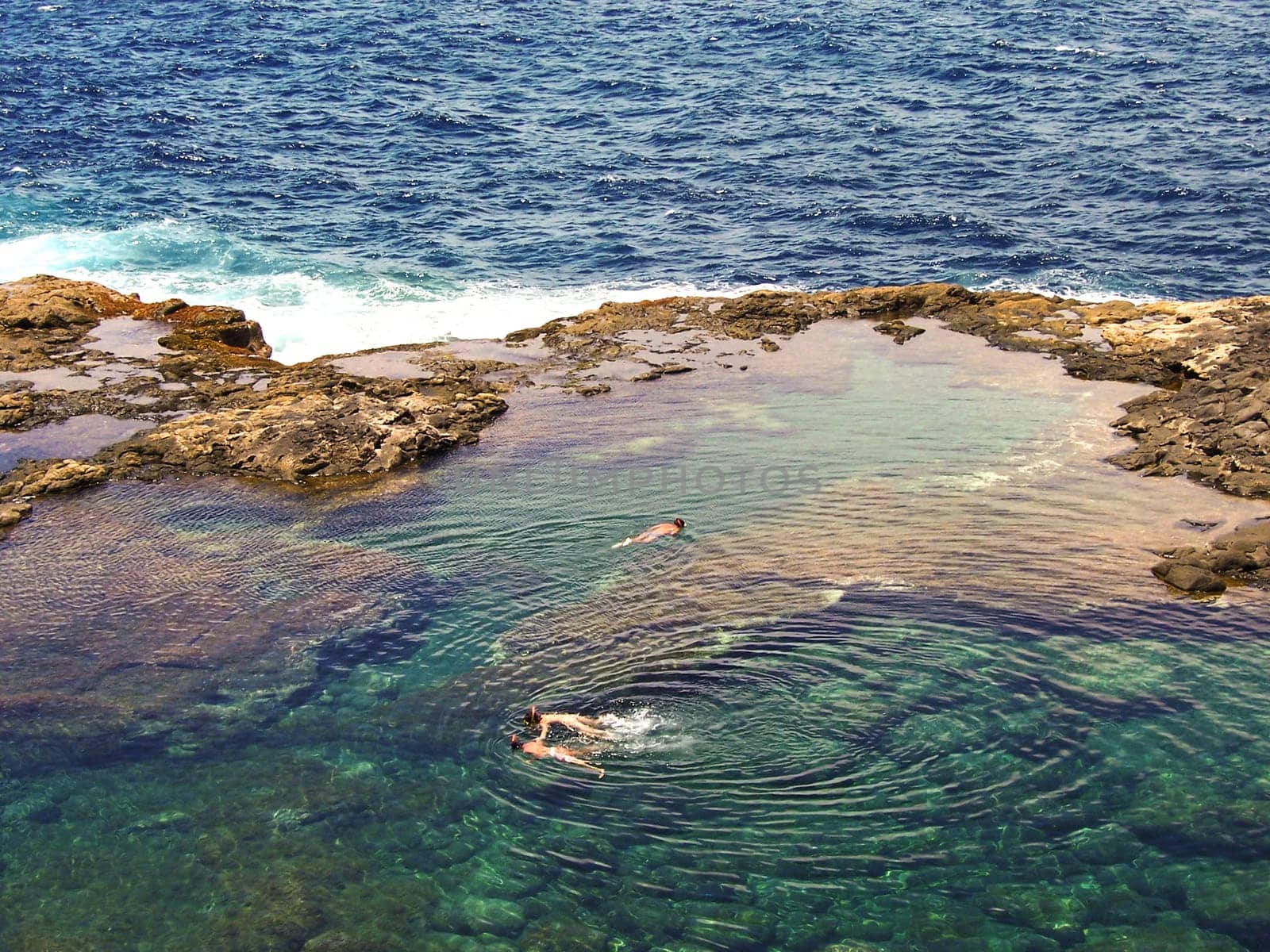 people diving in a natural basin in the rocks coastline of Lanzarote
