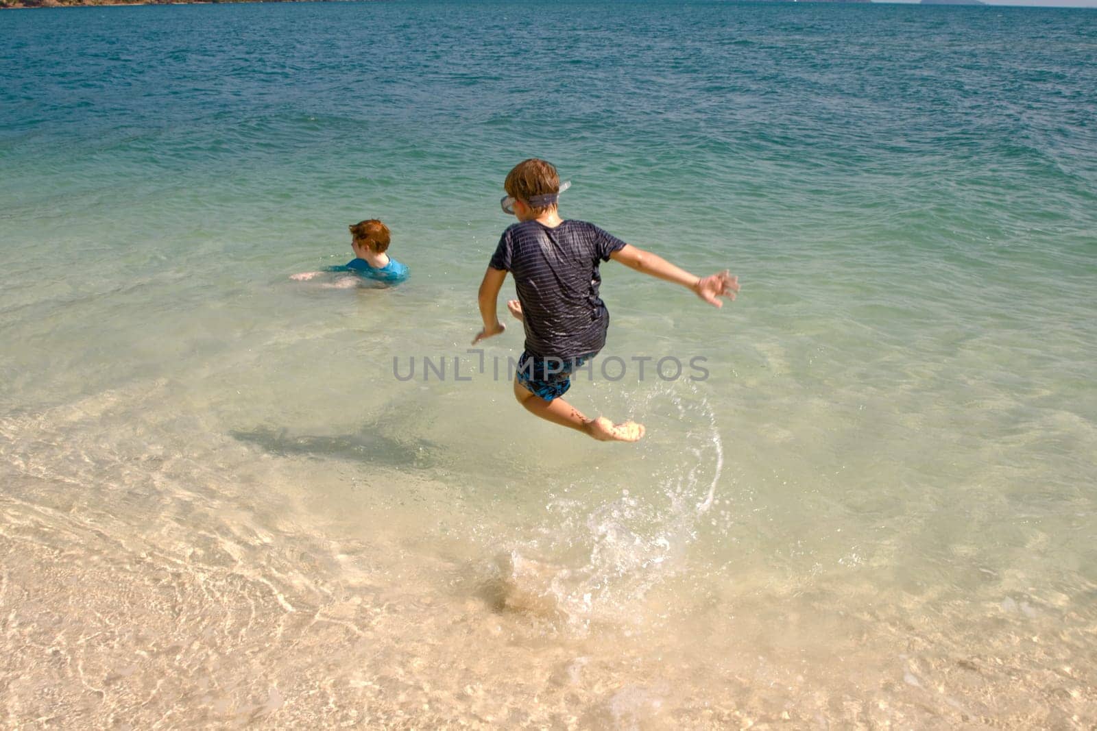 brothers are jumping and playing on a idyllic beach and having fun in the water