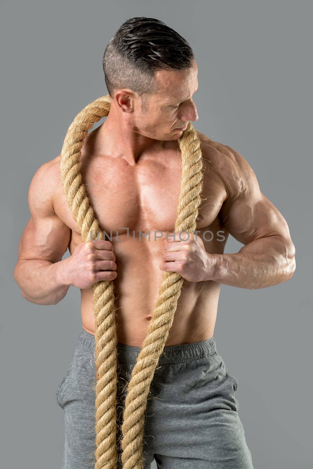 Powerful athletic man with great physique. Strong bodybuilder holding a big rope.