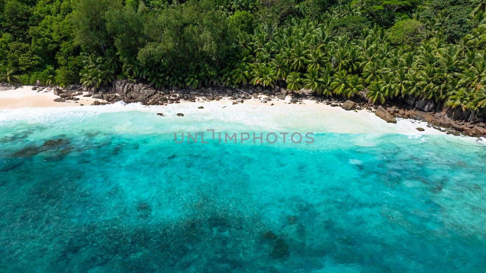 Waves gently wash over the white sand beach surrounded by tropical vegetation. Anse Intendance. Seychelles, Mahe.
