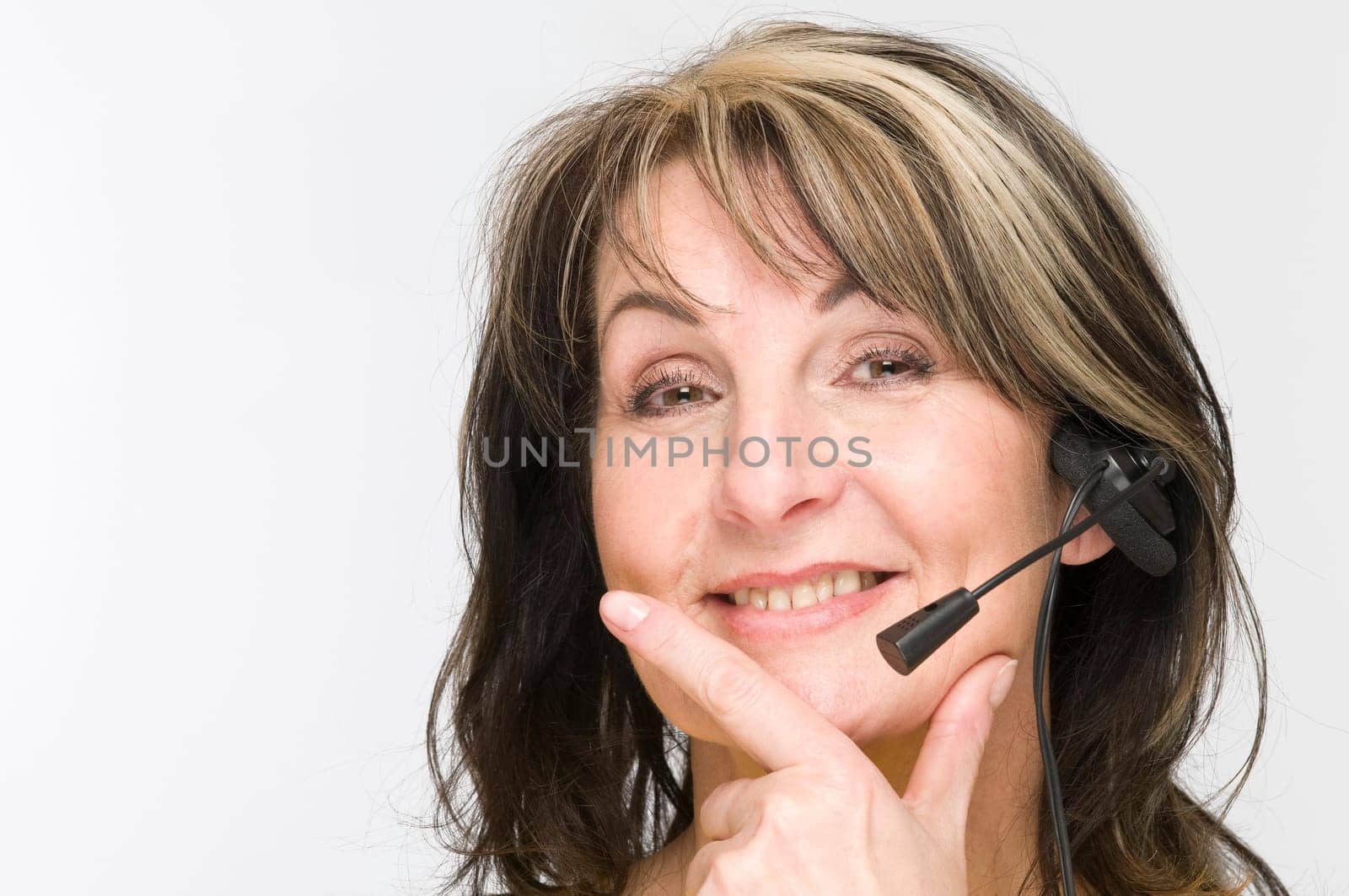 Frontal head portrait of a middle-aged woman with headphone set against a white background thumb and index finger touching the chin.