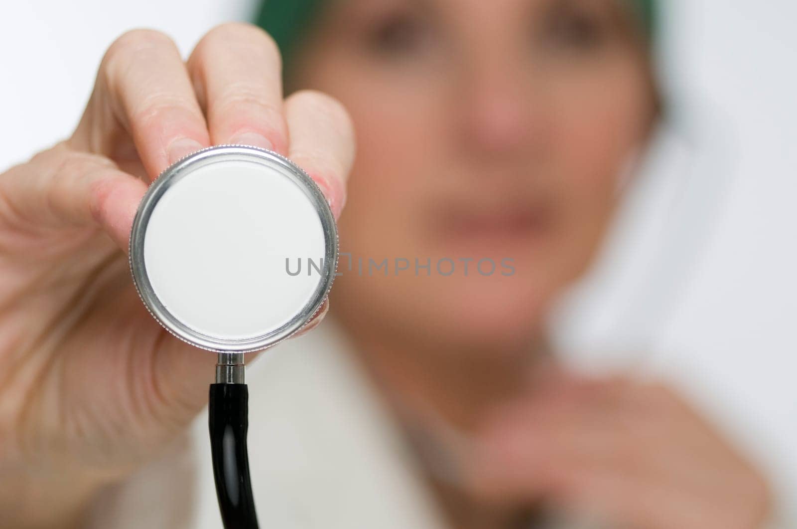 Doctor in the blurred background holds the membrane of a stethoscope in the direction of the camera