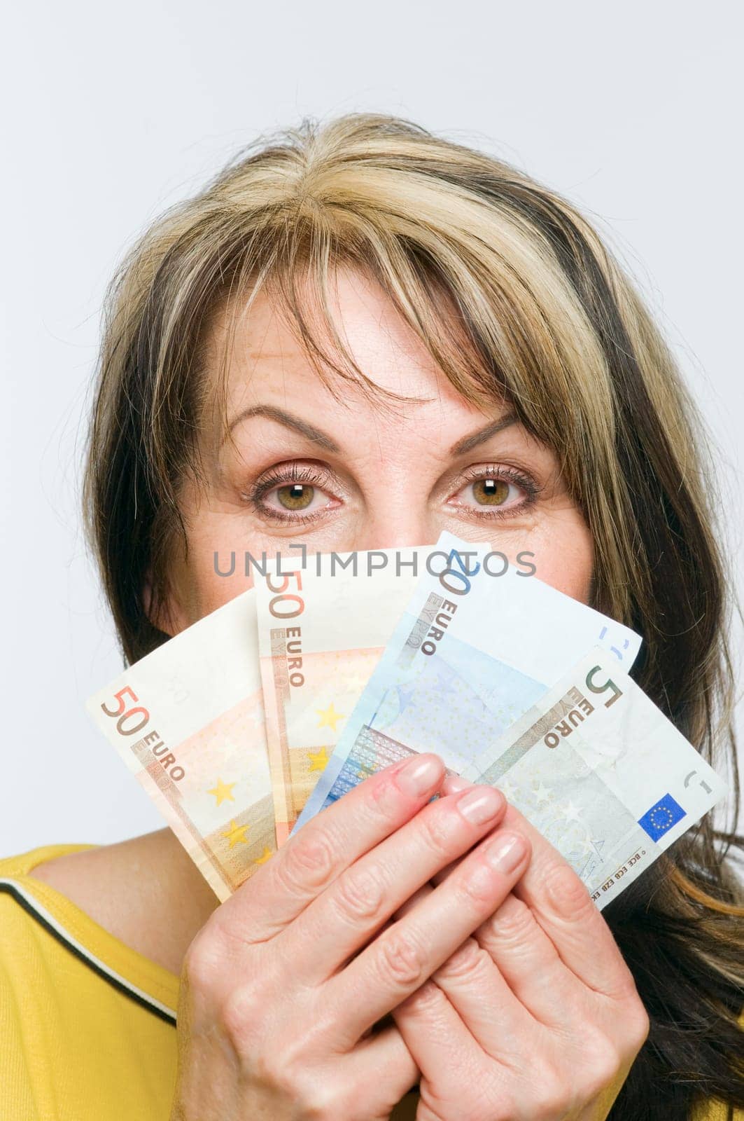 Frontal head-and-shoulder view of a middle-aged woman holding fanned out banknotes in front of her mouth and nose against a white background.