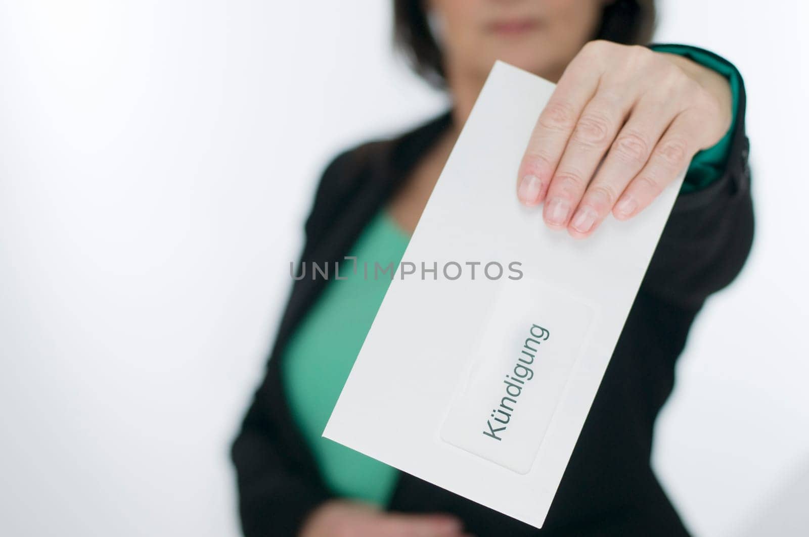 Upper body view of a middle-aged woman in the blurred background holds an envelope into the camera