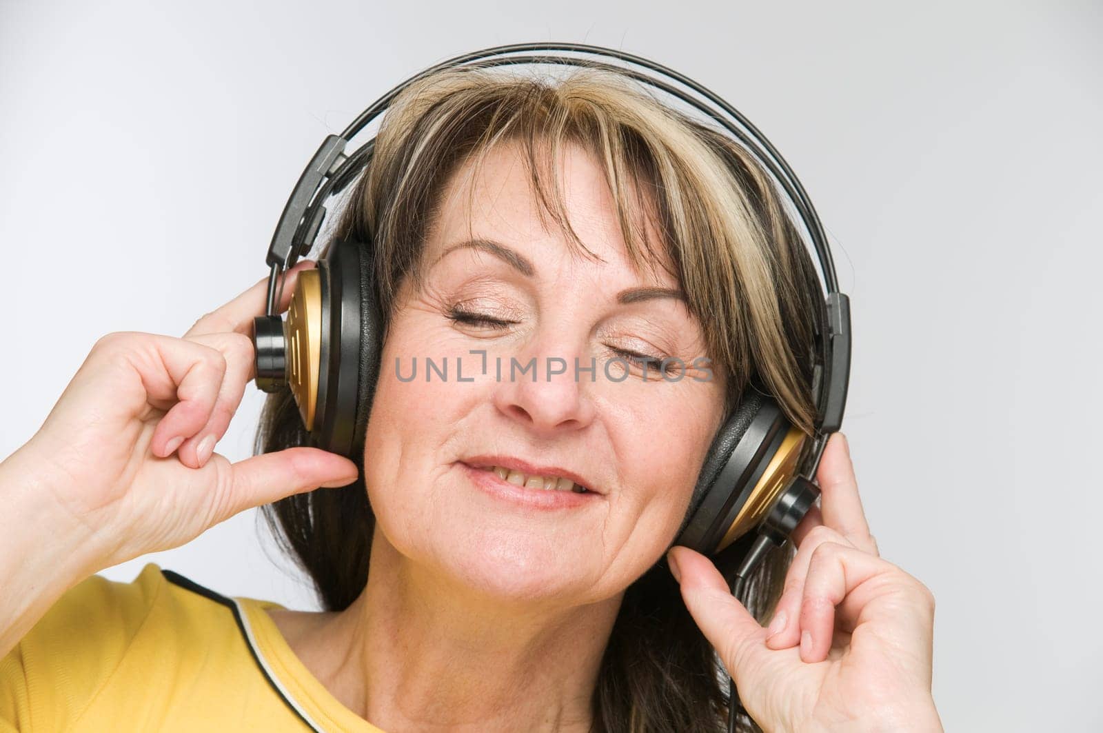 Head-and-shoulder view of a middle-aged woman with closed eyes and headphones against a white background.