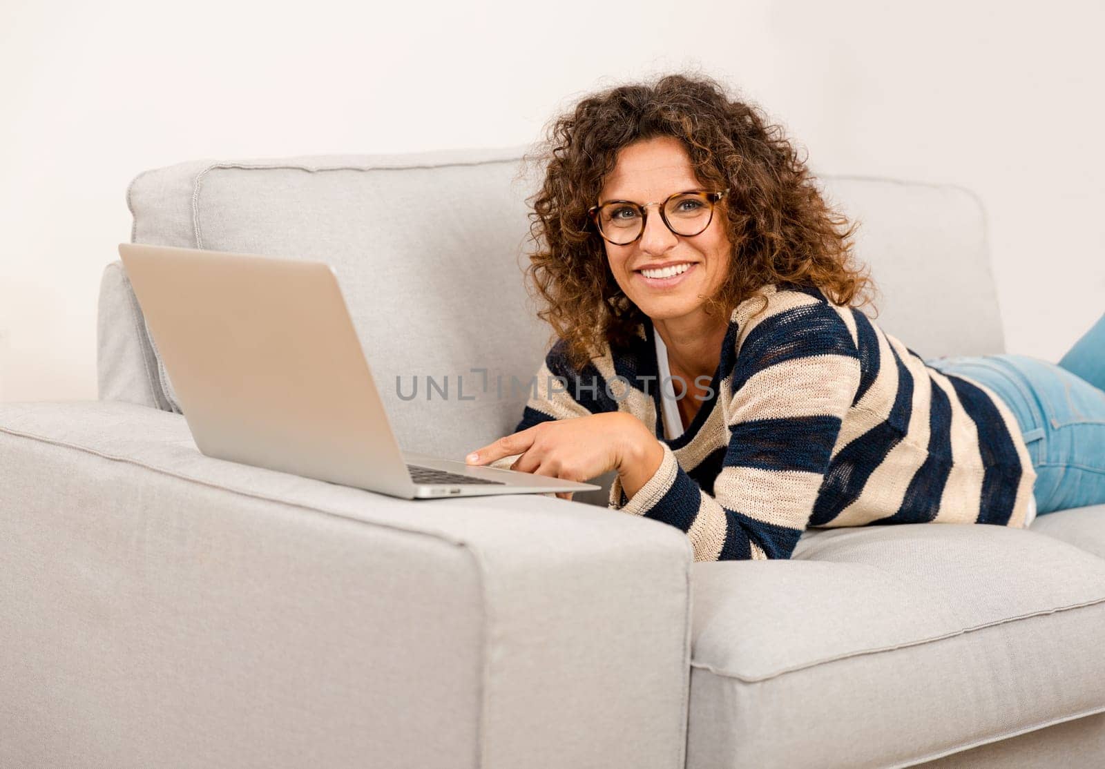 Beautiful woman at home lying on the sofa and working with a laptop