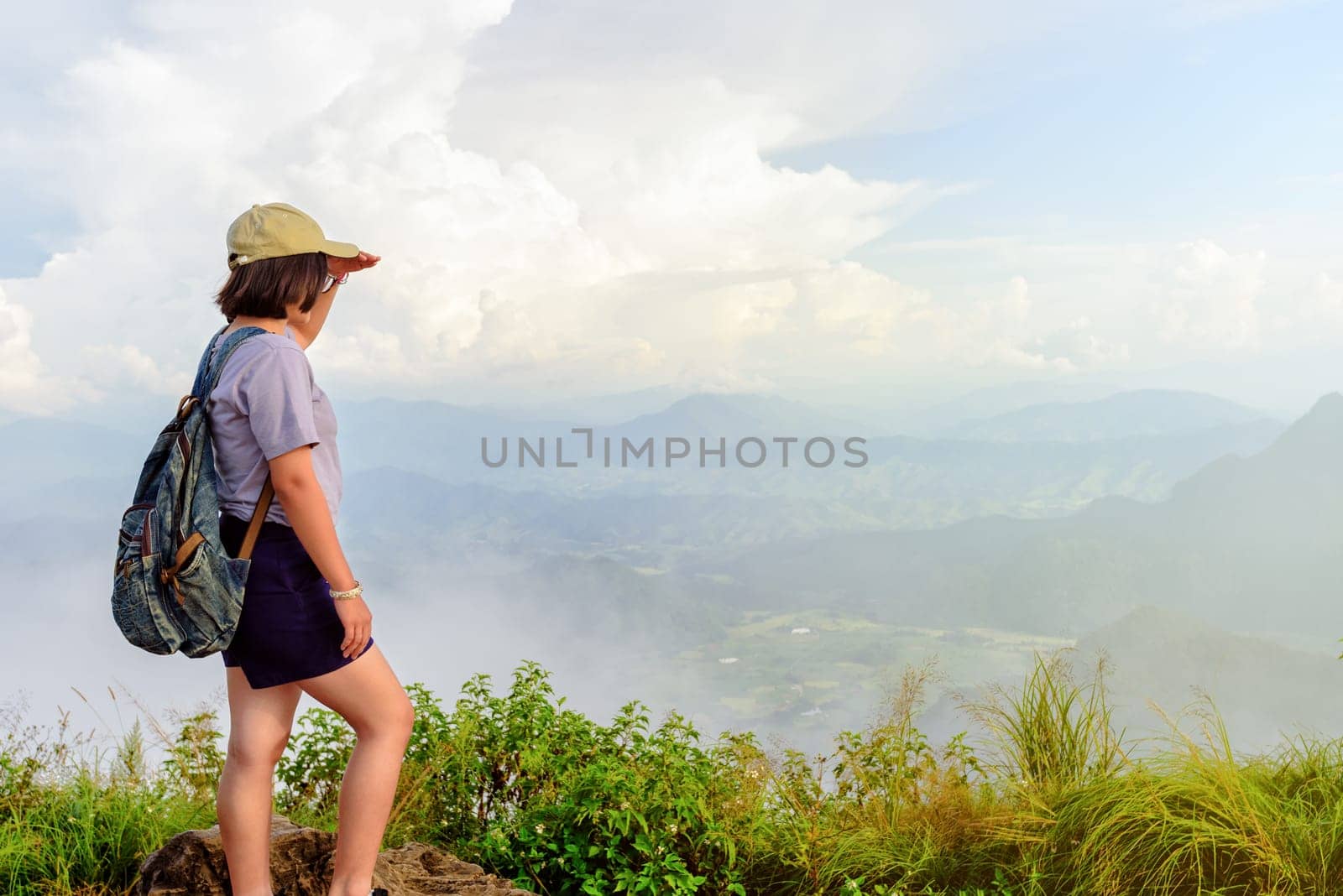 Traveler teens girl hiker wear cap and glasses with backpack looking beautiful nature landscape on high mountain at viewpoint of Phu Chi Fa Forest Park during sunset in Chiang Rai Province Thailand